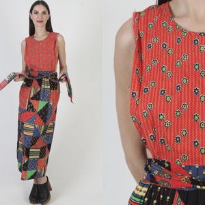 Può includere: Abito senza maniche in stile vintage con corpetto rosso a fantasia floreale e gonna patchwork. L'abito presenta una fascia abbinata e viene indossato con stivaletti neri. La gonna presenta una varietà di motivi geometrici multicolori.