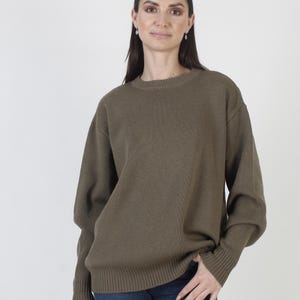 Puede incluir: Su&eacute;ter verde oliva con cuello redondo y mangas largas. El su&eacute;ter tiene una textura acanalada en los pu&ntilde;os y el dobladillo. La modelo lleva vaqueros azules.