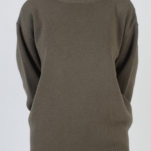 Puede incluir: Su&eacute;ter verde oliva con cuello redondo y mangas largas. El su&eacute;ter tiene un dobladillo acanalado y un ajuste relajado. La tela parece ser un tejido de peso medio, adecuado para climas m&aacute;s fr&iacute;os. El modelo lleva vaqueros azules.