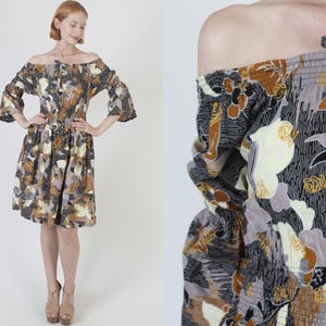 Könnte beinhalten: Ein kurzes, schulterfreies Kleid mit einem Blumendruck in Braun-, Beige- und Schwarztönen. Das Kleid hat eine taillierte Taille und einen fließenden Rock.