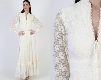 May include: Ivory-colored vintage dress with long lace sleeves and a high collar. The dress features a fitted bodice, a lace panel down the front, and a flowing skirt with a ruffled hem. The dress has a button-up front and a tie at the neckline.