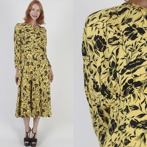 May include: A yellow midi dress with a black floral print. The dress has a button-up front and long sleeves.