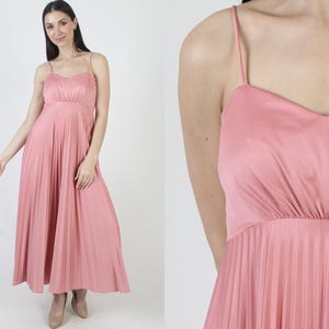 Peut inclure: Une longue robe maxi plissée rose avec des bretelles fines. La robe a un décolleté en cœur et un corsage ajusté.