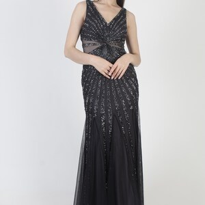 May include: A sleeveless black evening gown with a V-neckline and a flowing skirt. The bodice and upper skirt are embellished with sparkling sequins, creating a radiant effect. The dress features a sheer panel at the waist.