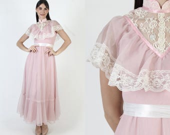 May include: A vintage pink maxi dress with a high collar and short, sheer sleeves. The dress features white lace detailing on the bodice and sleeves, a white ribbon belt, and a flowing skirt. The dress is a romantic, feminine style.