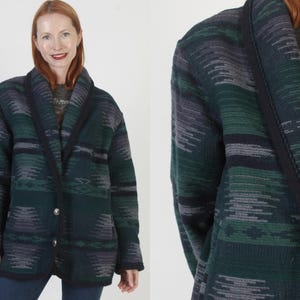 Puede incluir: Un cárdigan estampado en verde, gris y azul marino con cuello chal y dos botones plateados. El suéter tiene un diseño geométrico y lo lleva una persona en la imagen.