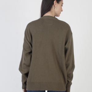 Puede incluir: Su&eacute;ter verde oliva con dobladillo y pu&ntilde;os acanalados. El su&eacute;ter de manga larga tiene cuello redondo y corte holgado. La vista trasera del su&eacute;ter se muestra sobre un fondo blanco. El su&eacute;ter est&aacute; hecho de un material de punto suave.