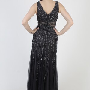 May include: A black formal gown with a V-neckline and a flowing skirt. The bodice and upper skirt are embellished with vertical rows of sequins. The dress features a sheer panel at the waist and a tulle overlay.