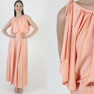 Peut inclure: Une robe longue pêche avec une jupe plissée et un corsage froncé. La robe présente un design sans manches avec de fines attaches aux épaules et une taille cintrée. Le tissu a un aspect doux et fluide, adapté aux événements formels.