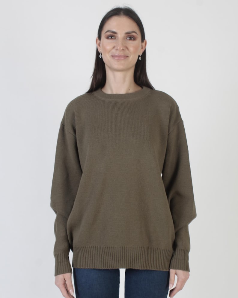 Puede incluir: Un su&eacute;ter verde oliva con cuello redondo y mangas largas. El su&eacute;ter tiene un dobladillo y pu&ntilde;os acanalados. La modelo lleva vaqueros azules. El fondo es blanco liso.