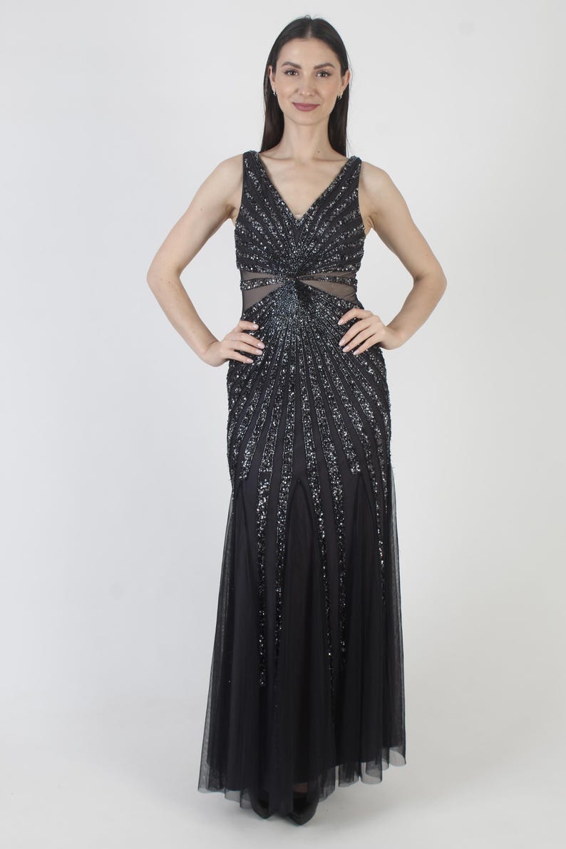 May include: A black formal gown with a V-neckline and a fitted bodice. The bodice and upper skirt are embellished with sparkling sequins in a radiating pattern. The lower skirt is a flowing, sheer fabric. The dress is sleeveless.