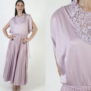 Könnte beinhalten: Vintage-Kleid in Lavendel mit plissiertem Rock und zartem Spitzenkragen. Das Kleid hat ein drapiertes Oberteil und einen passenden Gürtel. Das Kleid ist aus seidigem Material und hat kurze Ärmel. Ein klassischer, eleganter Stil.
