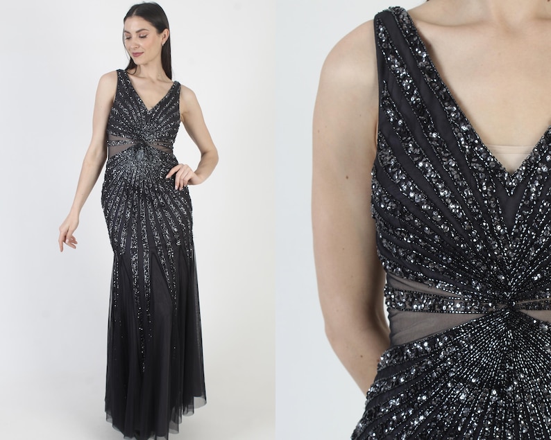 May include: A black formal gown with a V-neckline and intricate sequin and bead embellishments. The dress features a fitted bodice with a sheer midriff and a flowing, floor-length skirt. The design includes a detailed, radiating pattern.