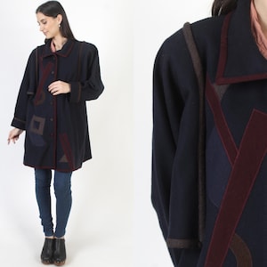 May include: A navy blue coat with geometric shapes in burgundy, brown, and navy. The coat has a button-up front, a collar, and long sleeves. The coat's design includes a burgundy trim and decorative shapes.