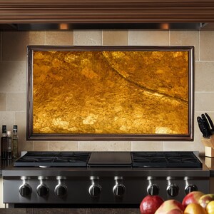May include: A stainless steel gas stove with five knobs and a black cast iron griddle. The stove is in front of a backsplash with a large, framed piece of amber-colored stone.