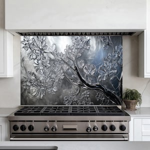 May include: A stainless steel stovetop with five burners and a black glass backsplash featuring a silver and grey embossed floral design.