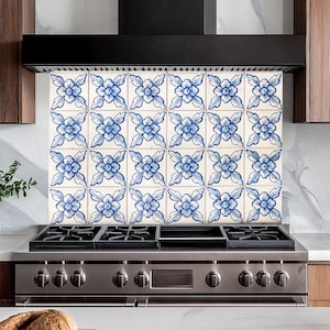 May include: A stainless steel stovetop with five burners and a black control panel. The stovetop is in front of a white tiled backsplash with a blue and white floral pattern.