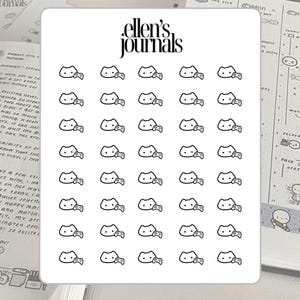 Puede incluir: Una hoja de pegatinas con un patrón repetido de una cara de gato con pajarita y un mando de videojuegos. Las pegatinas son blancas con contornos negros y el texto "ellen's journals" en la parte superior.