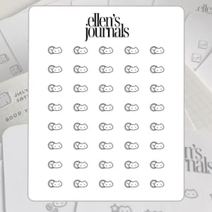 May include: A sheet of stickers featuring a repeating pattern of a cat face with a closed eye and a small circle. The stickers are black and white and have the text "ellen's journals" at the top.