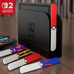 May include: A black Nintendo Switch console with a red and white controller attached. Several colourful controllers are displayed in front of the console, including purple, yellow, red, and blue designs. The Nintendo Switch logo is visible.