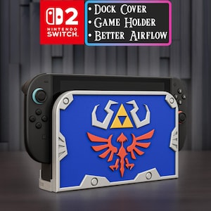 Peut inclure: Un cache-dock pour Nintendo Switch avec un design bleu, argenté et orange. Le cache présente un motif de bouclier avec le texte "Dock Cover, Game Holder, Better Airflow". Le logo Nintendo Switch est visible.