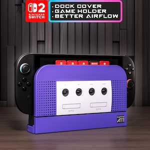May include: A purple and white Nintendo Switch dock cover featuring a GameCube-inspired design with four controller ports and two memory card slots. The text reads: DOCK COVER, GAME HOLDER, BETTER AIRFLOW, NINTENDO SWITCH, and Graphics by ATi.