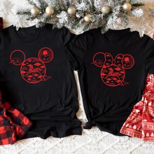 May include: Black t-shirts with red graphic designs featuring a horse and clouds in a Mickey Mouse head shape. Red and black plaid pajama pants and red pajama pants with white bear and tree patterns are also visible.