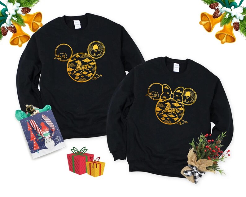 May include: Two black sweatshirts with a gold design featuring a horse, clouds, and sun, arranged in a Mickey Mouse head shape. Festive decorations, including bells and gifts, surround the sweatshirts.