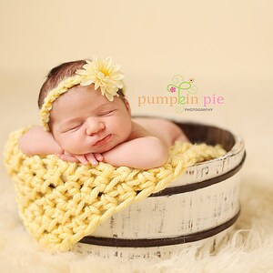 Op de afbeelding: Een slapende babymeisje met een geel gehaakt hoofdband met een gele bloem erop, liggend in een witte houten emmer met een geel gehaakt dekentje. De emmer staat op een wit pluche oppervlak. De tekst "pumpkin pie photography" staat in de rechterbovenhoek van de afbeelding.