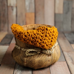 May include: A handcrafted, rustic basket with a woven design, featuring a mustard yellow crocheted edge. The basket is adorned with a natural rope tie. The background is a wooden plank surface.