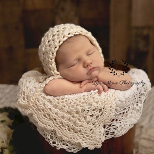Può includere: Un neonato che indossa un cappello di uncinetto bianco e una coperta di uncinetto bianca, dorme in un cesto di legno.