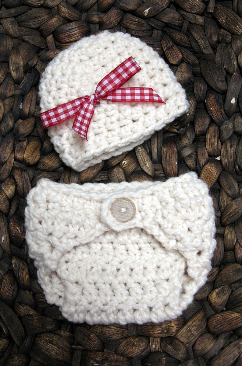 May include: A white crocheted baby hat with a red and white gingham bow. The hat is lying on a woven brown basket.