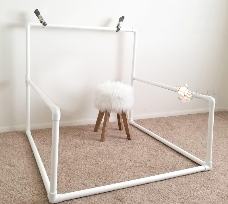 May include: White PVC pipe backdrop stand with a white furry stool in the center. The stand is assembled in a square shape with a top bar for hanging backdrops.