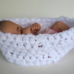May include: A white crocheted baby nest with a doll inside. The nest is made of a soft, fluffy yarn and has a delicate, lacy pattern.