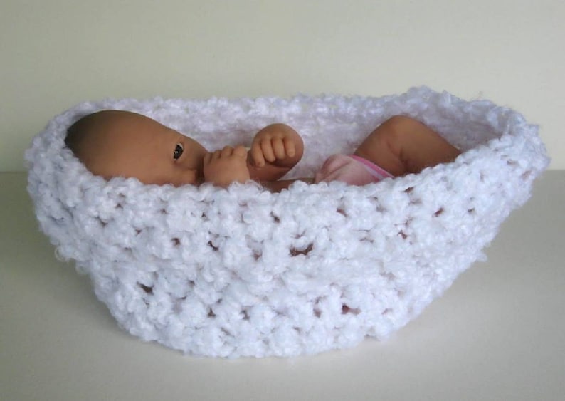 May include: A white crocheted baby nest with a doll inside. The nest is made of a soft, fluffy yarn and has a delicate, lacy pattern.