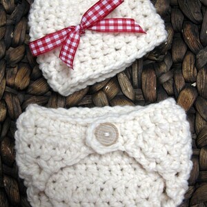 May include: A white crocheted baby hat with a red and white gingham bow and a white crocheted diaper with a wooden button.