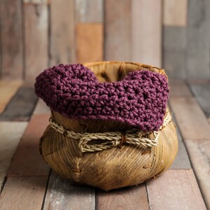May include: A purple crocheted baby blanket sits inside a woven basket with a natural brown finish.