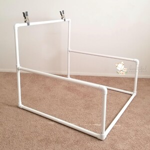 May include: White PVC pipe backdrop stand for photography. The stand is made of four sections of pipe that are connected together to form a rectangular frame. The stand is about 3 feet tall and 4 feet wide. The stand is designed to hold a backdrop for photography.