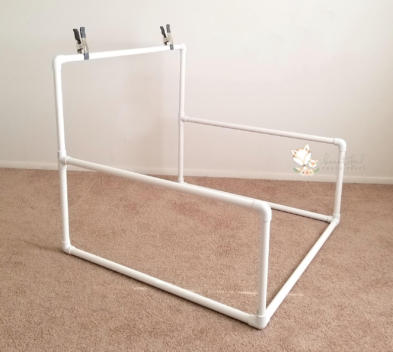May include: White PVC pipe backdrop stand for photography. The stand is made of four sections of pipe that are connected together to form a rectangular frame. The stand is about 3 feet tall and 4 feet wide. The stand is designed to hold a backdrop for photography.