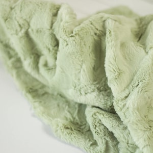 May include: A soft, plush blanket in a light green color. The blanket has a textured, fluffy surface and is made of a soft, comfortable material.