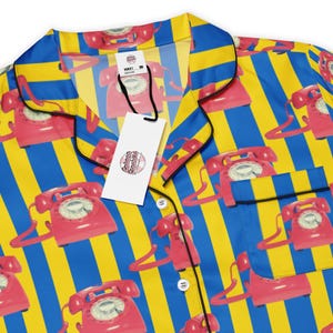 May include: A blue and yellow striped pajama top with a repeating pattern of red rotary phones. The top has a black collar and black buttons.