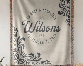 Puede incluir: Una manta tejida de color crema con adornos decorativos de color gris oscuro en las esquinas y texto personalizado que dice Gregory & Annabelle, The Wilsons, EST SEPTEMBER 9, 2025. La manta tiene un borde con flecos multicolores.