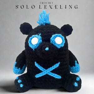 Puede incluir: Un oso negro de ganchillo con detalles azules, incluyendo los ojos, los pies y un mechón de pelo. El oso tiene una 'X' azul en el pecho. El texto "SOLO LEVELING" y "CROCHET" se encuentra en la parte superior de la imagen.
