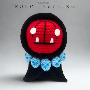 Puede incluir: Peluche de ganchillo hecho a mano de un personaje de Solo Leveling. El peluche tiene una cabeza roja con ojos blancos y pequeños dientes blancos. Tiene una capucha negra y un cuello azul con detalles azules. Las palabras "CROCHET" y "SOLO LEVELING" están en la parte superior.