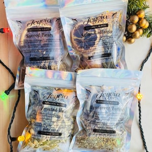 May include: Four iridescent pouches of Joyvia Co. botanical blends labeled Sacred Heart, Solar Radiance, Frosted Veil, and Evergreen Forest. Each clear bag contains dried herbs, citrus slices, and spices, with visible text detailing ingredients and small batch production.