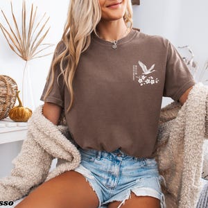 May include: A brown t-shirt with a white crane and flower design. The text "Where the wild things are" is printed on the shirt.