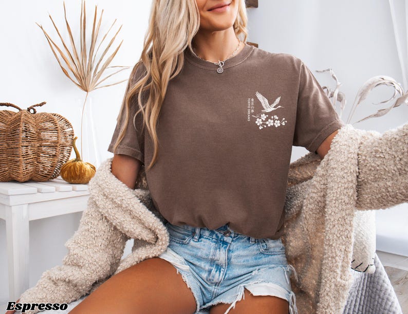 May include: A brown t-shirt with a white crane and flower design. The text "Where the wild things are" is printed on the shirt.