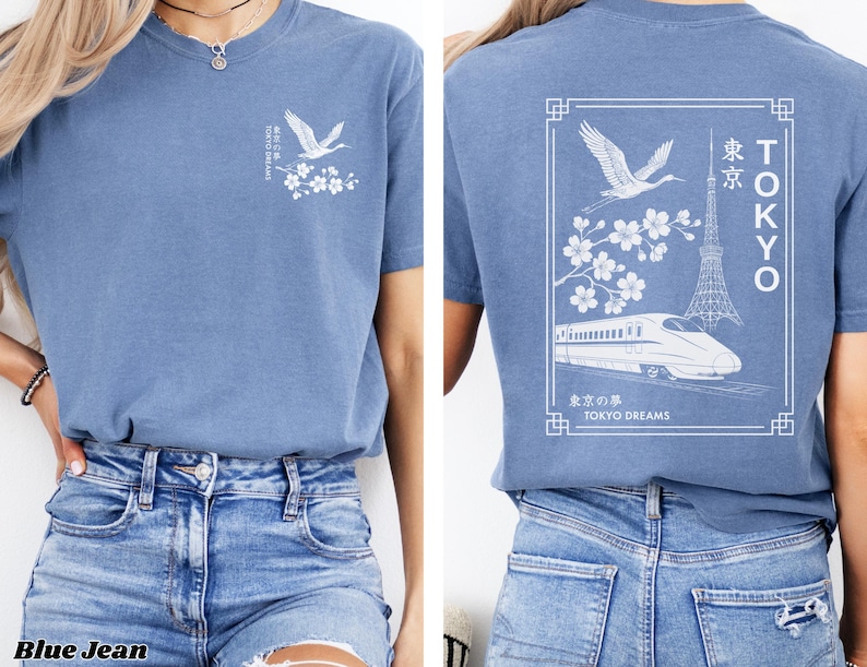 May include: A blue t-shirt with a white graphic design featuring a crane, cherry blossoms, a train, and the Tokyo Tower. The text on the shirt reads "TOKYO DREAMS" and "東京".
