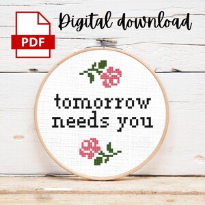 May include: A white embroidery hoop with the text "tomorrow needs you" in black lettering and two pink flowers with green stems.