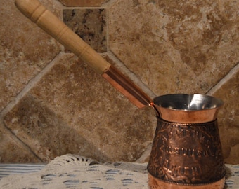 Cafetera turca de cobre con asa de madera. La taza mide poco menos de 10 cm de alto.